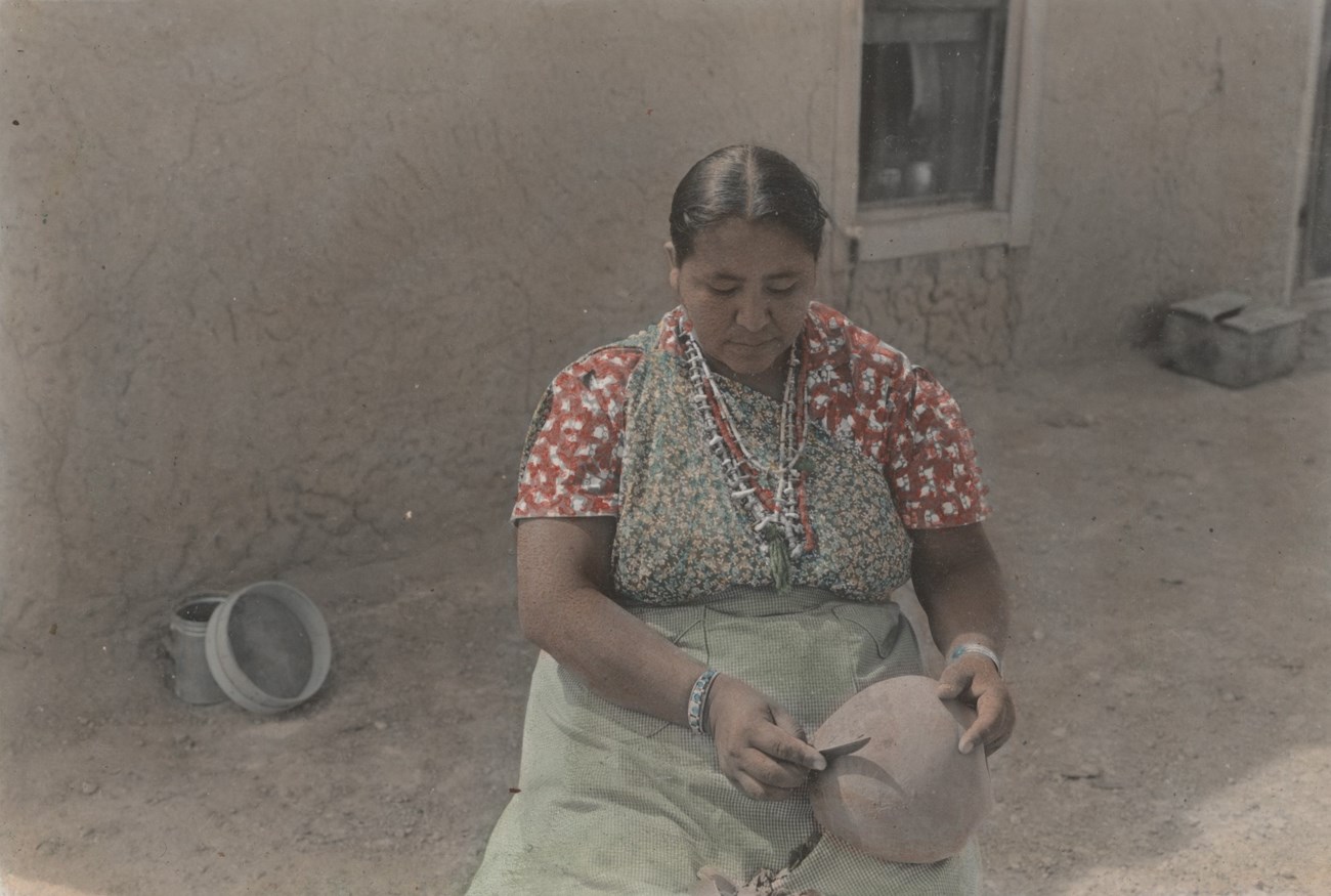 Legoria Tafoya sits using a knife to scrape at an unfired clay pot.