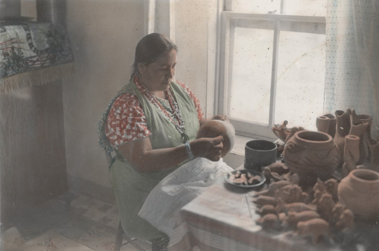 Legoria Tafoya sits in her house applying slip to a pot.