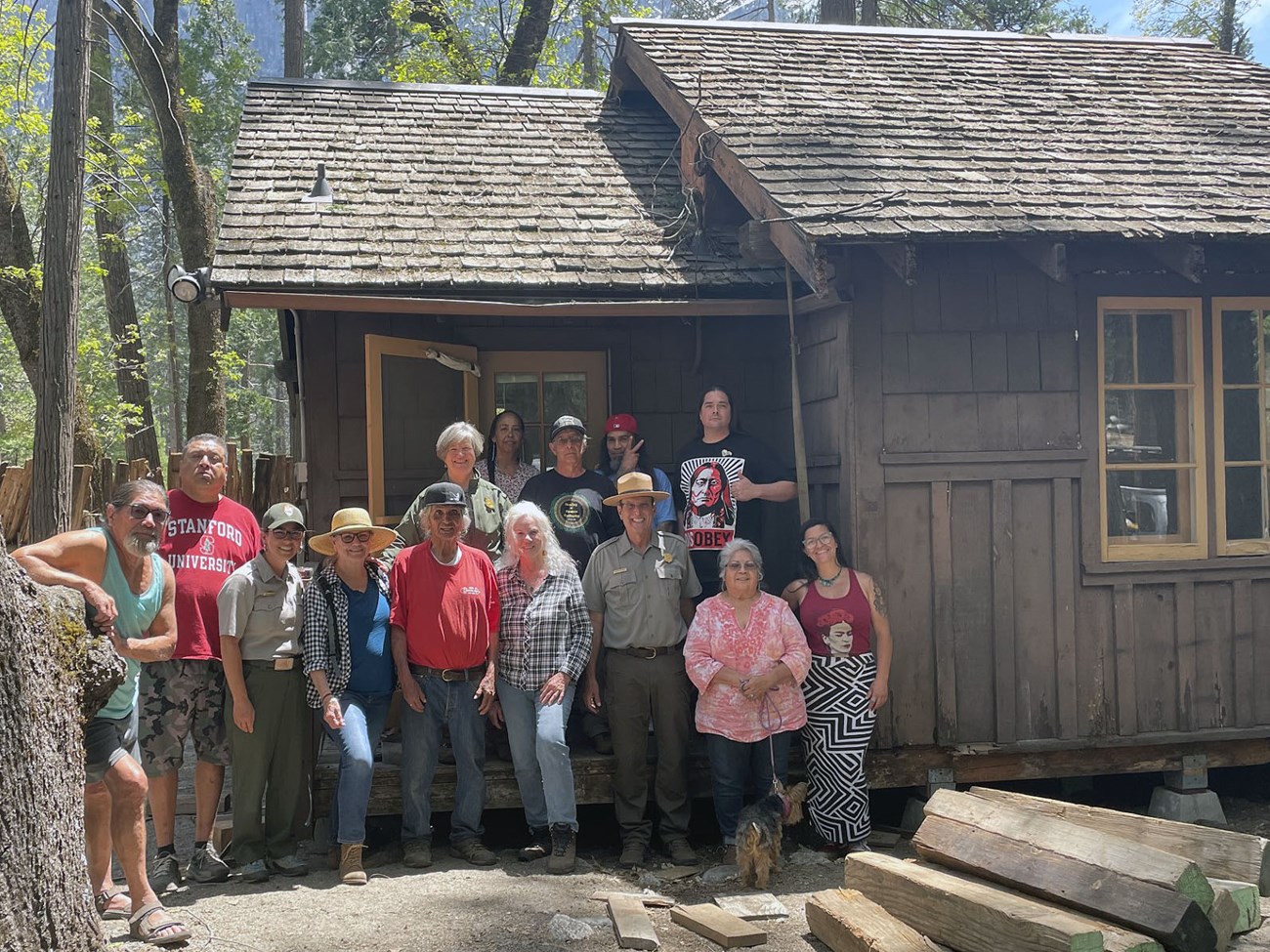 Group of indigenous people and national park service employees pose in front of wooden cabin