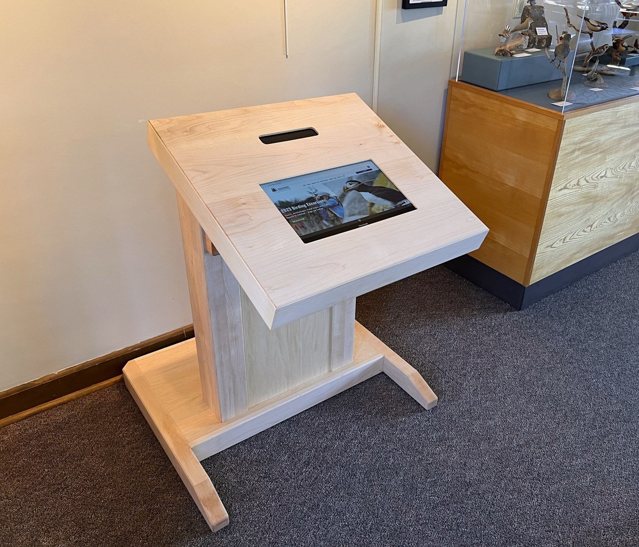 A wooden stand with an inset touch screen. The touch screen displays a program with a photo of a puffin and some text.