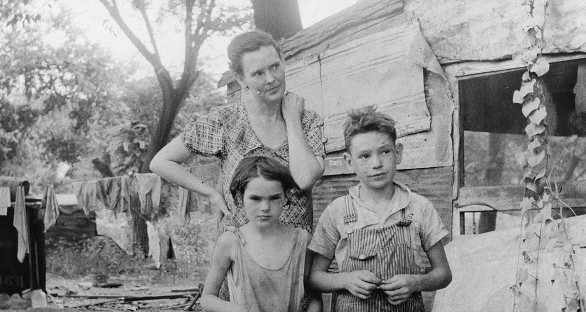 A black and white photo of a woman and kids dressed in raggedy clothes