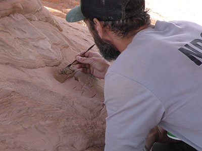 a ranger uses a small tool to press filling into carved graffiti