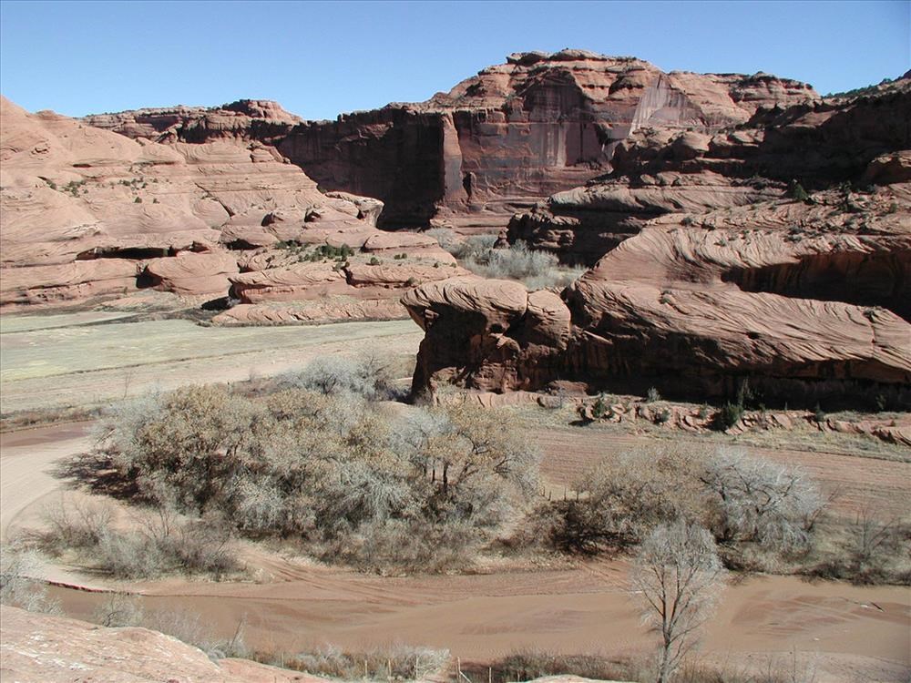 An extra wide shot of a barren, dry landscape, featuring red canyon walls and cliffs.