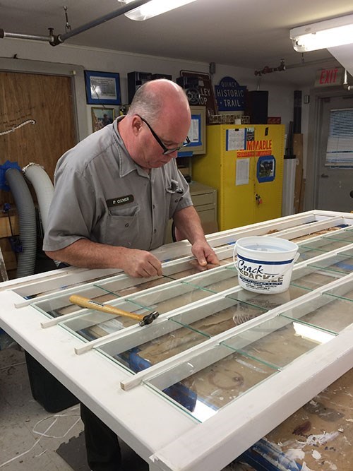 NPS staff replacing a window pane on a window laying on a worktable