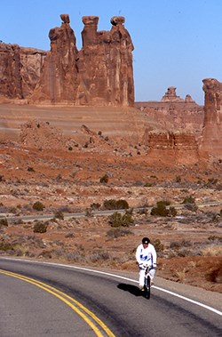 lt= a cyclist wearing white rides in front of rock formations