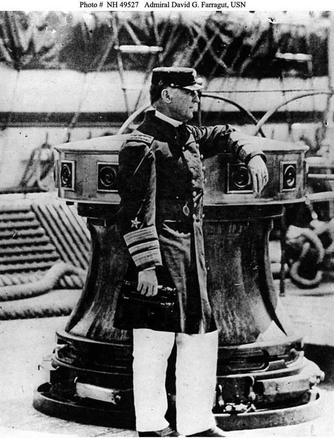 Admiral Farragut Black and white: A man is standing on a deck of a ship. His uniform shirt and hat are dark. His pants are white.
