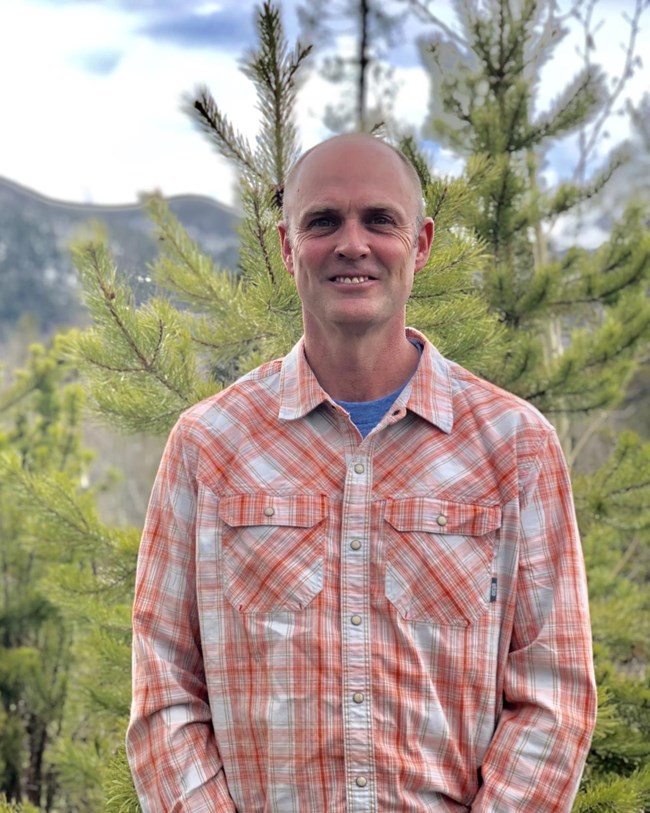 Biologist Andrew Ray wears a plaid shirt and smiles at the camera.
