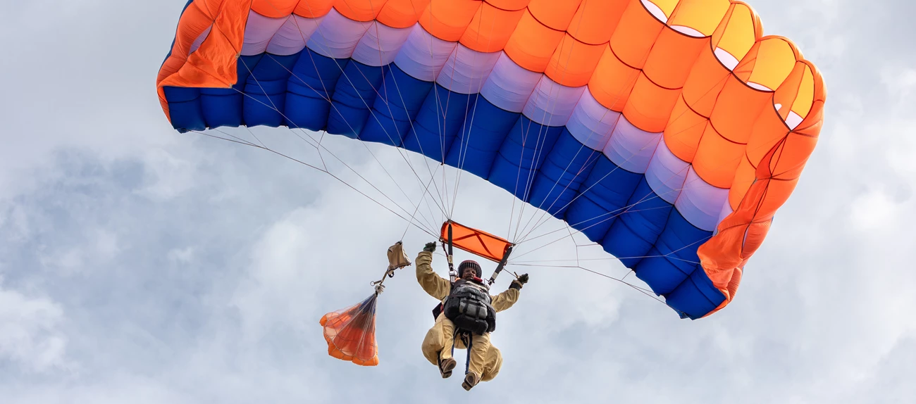 BLM Great Basin smokejumper A smokejumper under a red, white, and blue rectangular canopy floats down from sunny skies.