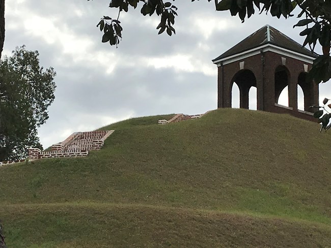 Brick stairs on a green hill lead up to a brick pavilion