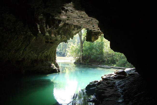 view from inside cave spring looking out at river, blue water and dark rocks at the mouth of the opening