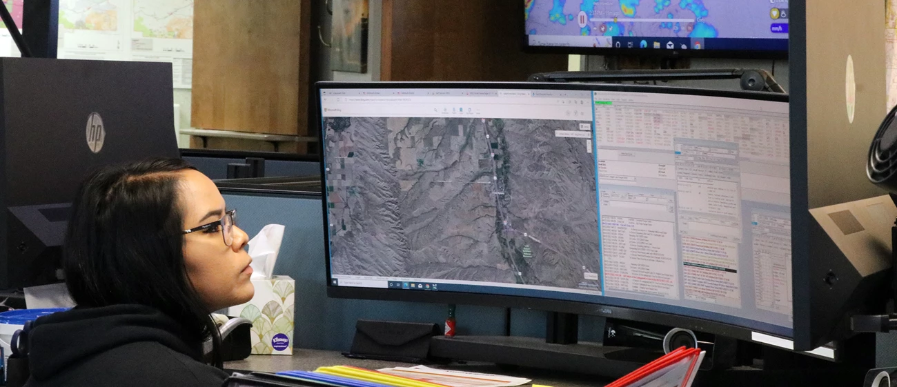 Dispatcher at work A woman sits in front of and looks at one of three computer screens.