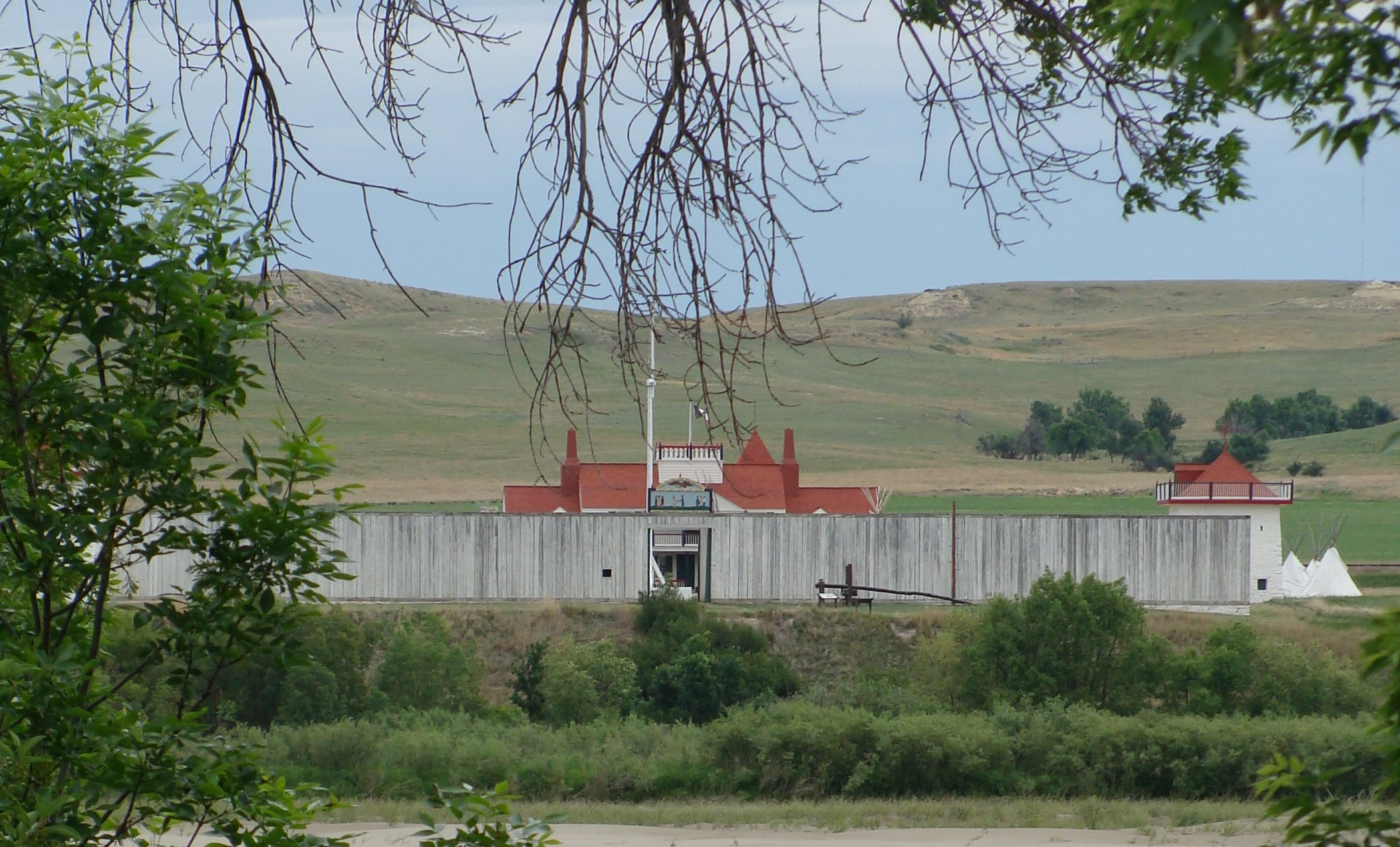 Grey and red wooden fort building among rolling, grassy hills.