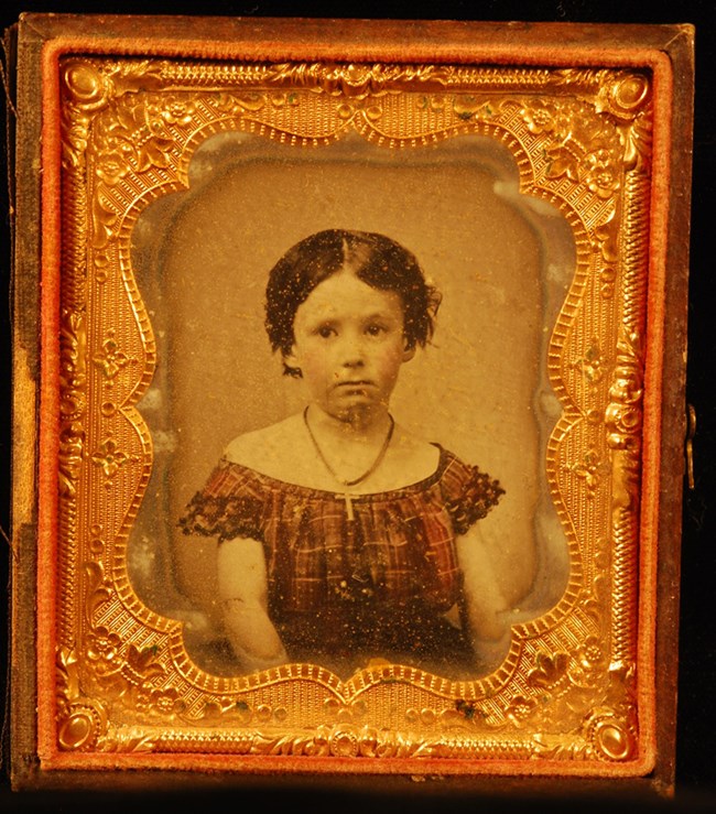 Tintype photograph of girl wearing a checkered dress and a cross necklace