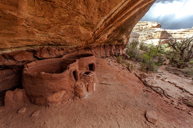 Ruins below an overhanging cliff in a valley.