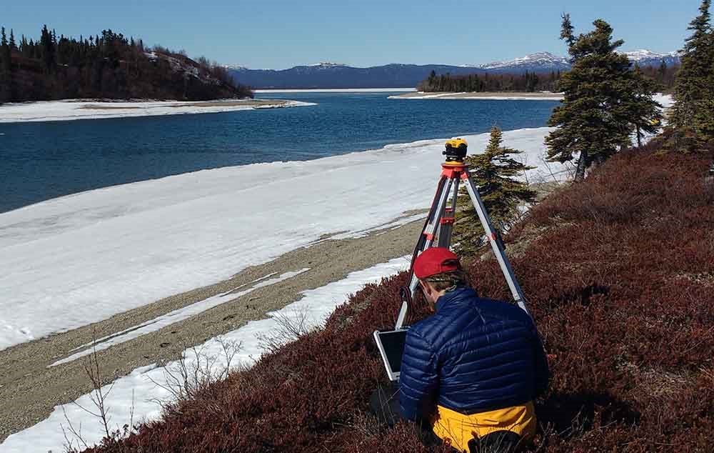 A researcher uses survey equipment along the lake edge.