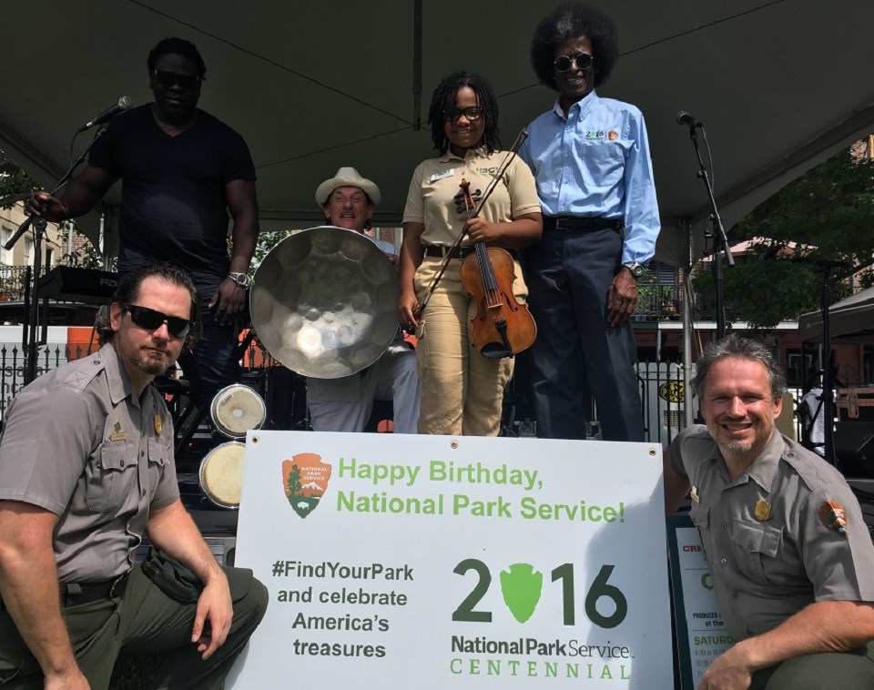 Park rangers and volunteers holding instruments and an NPS Centennial sign