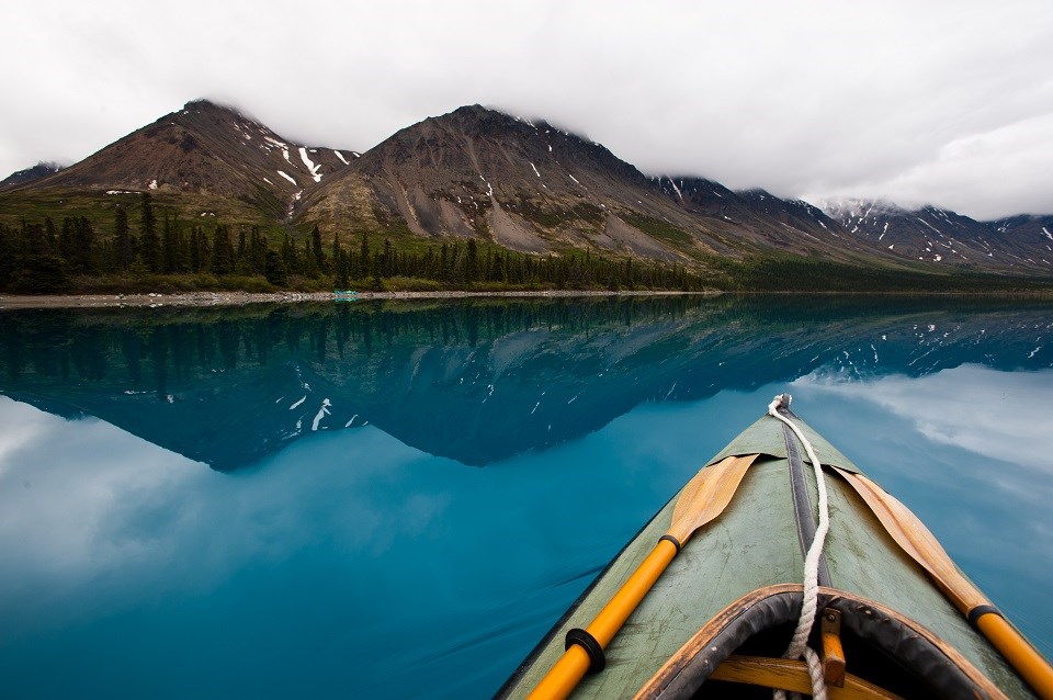 Bow of a kayak on a lake approaching mountains