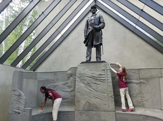 two interns cleaning a statue of Farragut at Saint-Gaudens. NPS photo