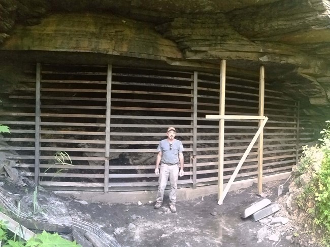 A man standing next to a mine portal with a large gate covering the entrance.