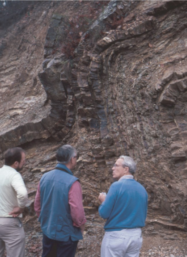 Photo 6.7 Ouachita Mountains three people standing in front of rock cliff with folded rock layers