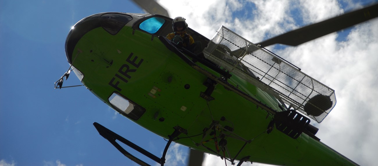 A view from below looking up in the sky at a person leaning out of a helicopter.
