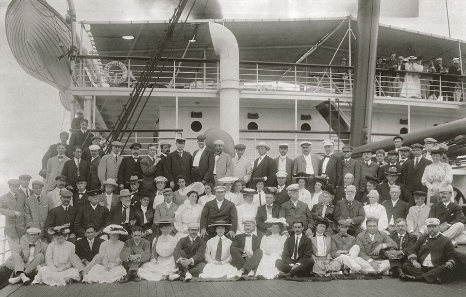 Several people sitting and standing for a photo on a ship deck