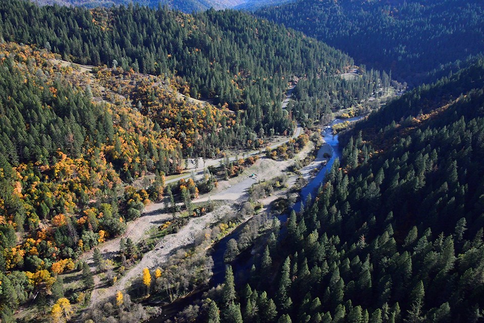 A blue river winds through a steep, tree-lined canyon