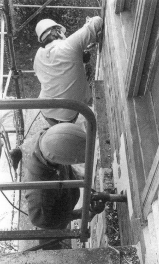 Two men on scaffolding removing paint from a wall.