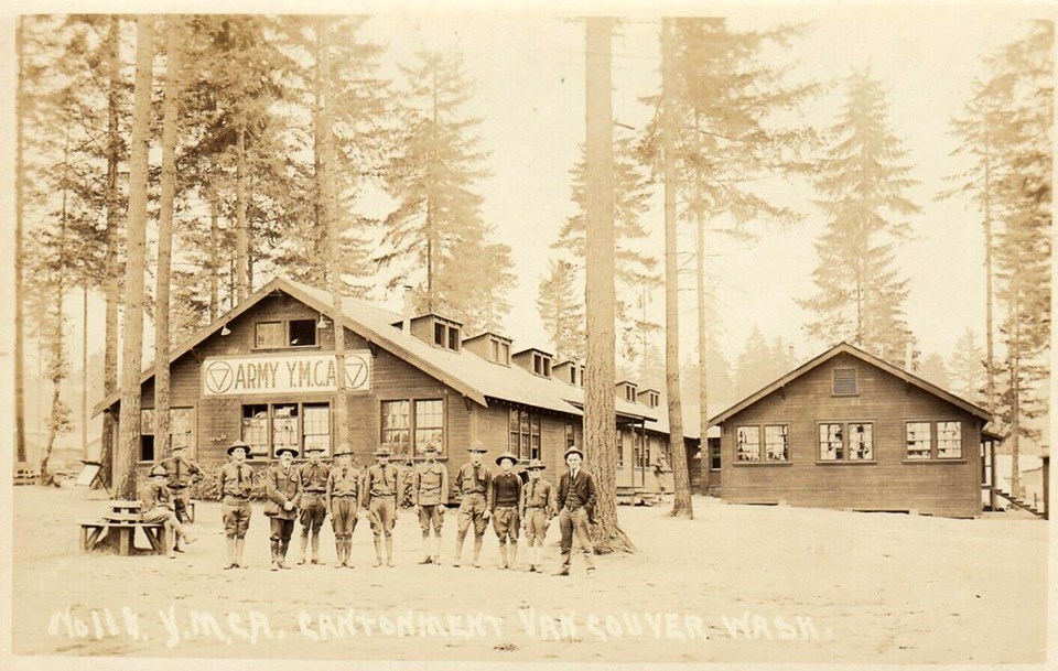 Black and white photo of men in military uniforms standing in front of a YMCA building in a forested area.
