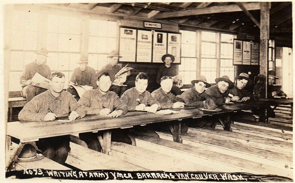 Black and white image of soldiers sitting at a long table writing letters.