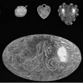 Large oval-shaped jewelry piece at bottom inscribed with cursive letter "A". On the left is an acorn-shaped jewelry piece. Two other pieces are heart-shaped, one with a cursive letter "L" inscribed.