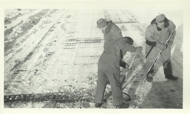 Black and white photo of men laying metal mat on snowy area