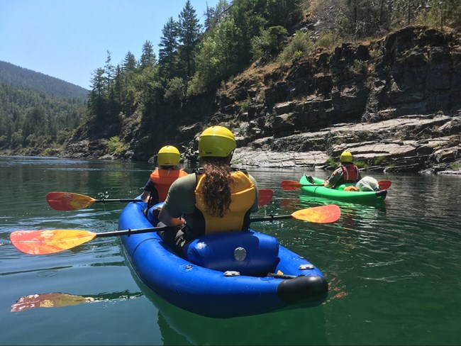 Two people kayaking in a bright blue boat on a calm green river.