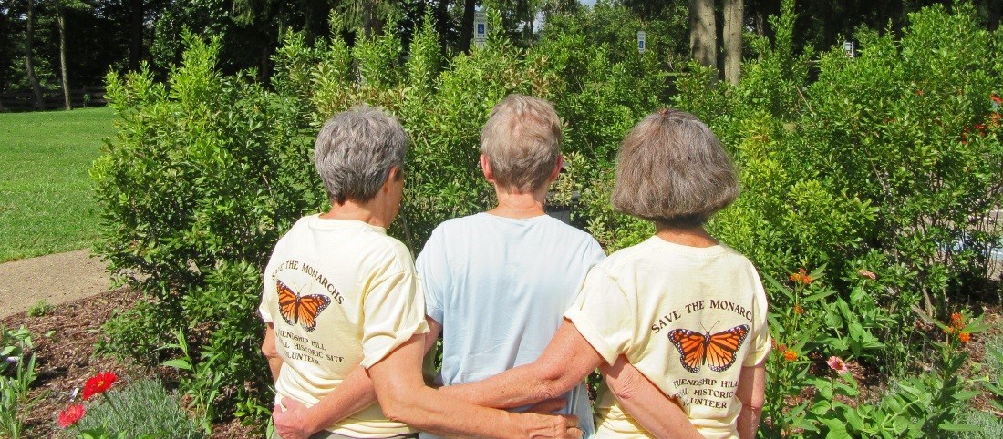 Three ladies wearing shirts that say "Save the Monarchs!" stand with their backs facing the camera