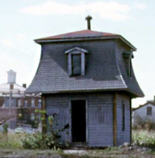 A tall old shed built in a victorian style with a distinctive squared-off roof.