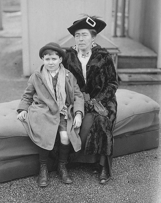 A woman in black sits next to a boy wearing a suit
