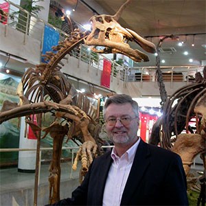scientist in museum hall with dinosaur skeleton