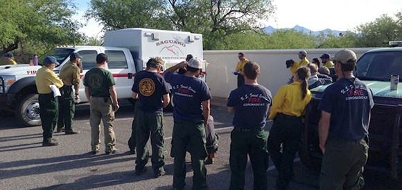 A group of firefighters gathers in a parking area for a briefing.