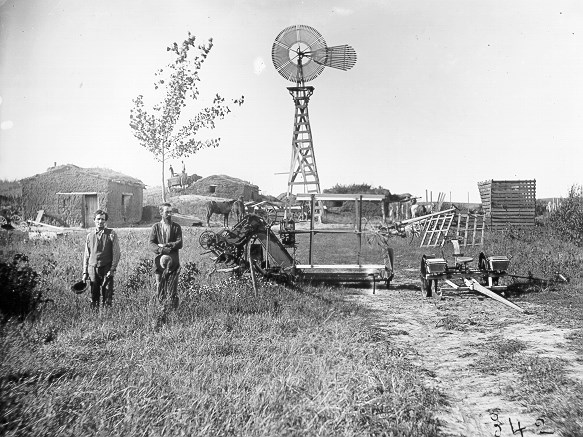 two men on their homestead in front of a windmill