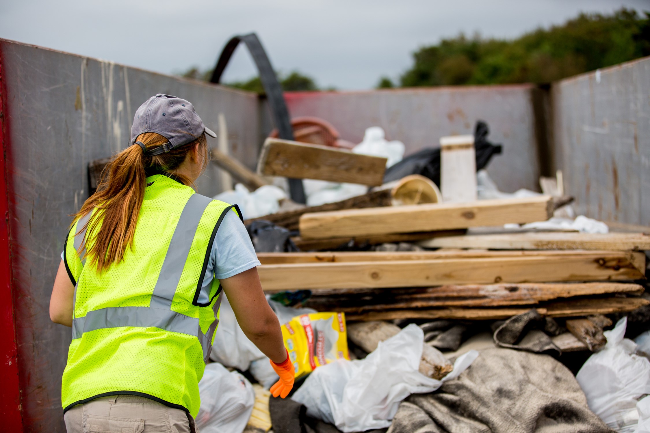 A volunteer in a fluorescent yellow safety vest throws debris from Assateague's beach into a dumpster.