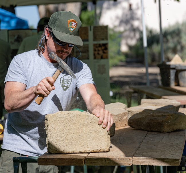 A Preservation worker chiseling a block of sandstone with a pick axe.