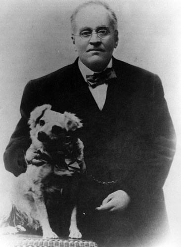 A black and white photo of a man in a suit with a dog.