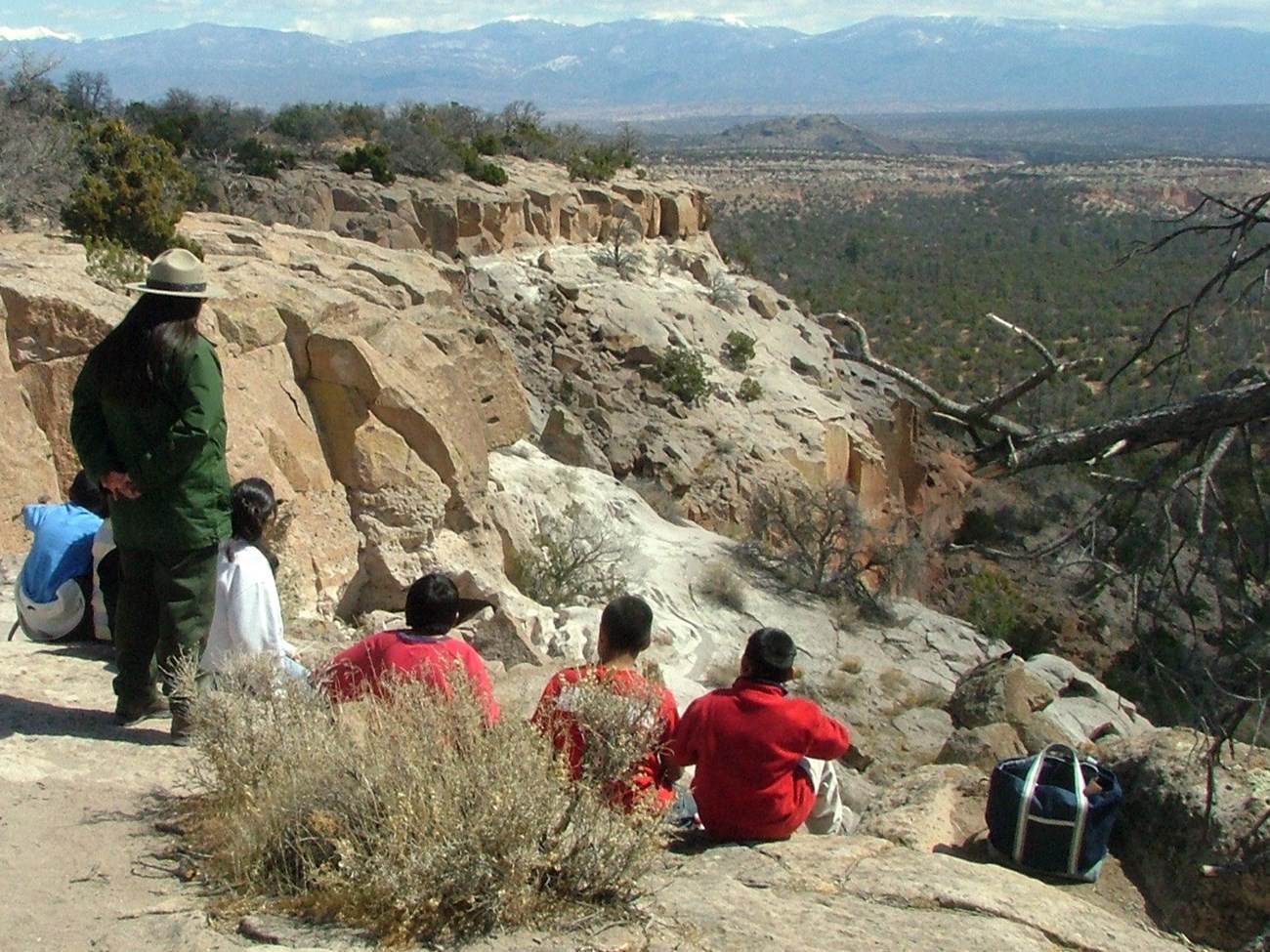 A park ranger and a group of children look out into the distance over a rocky landscape.