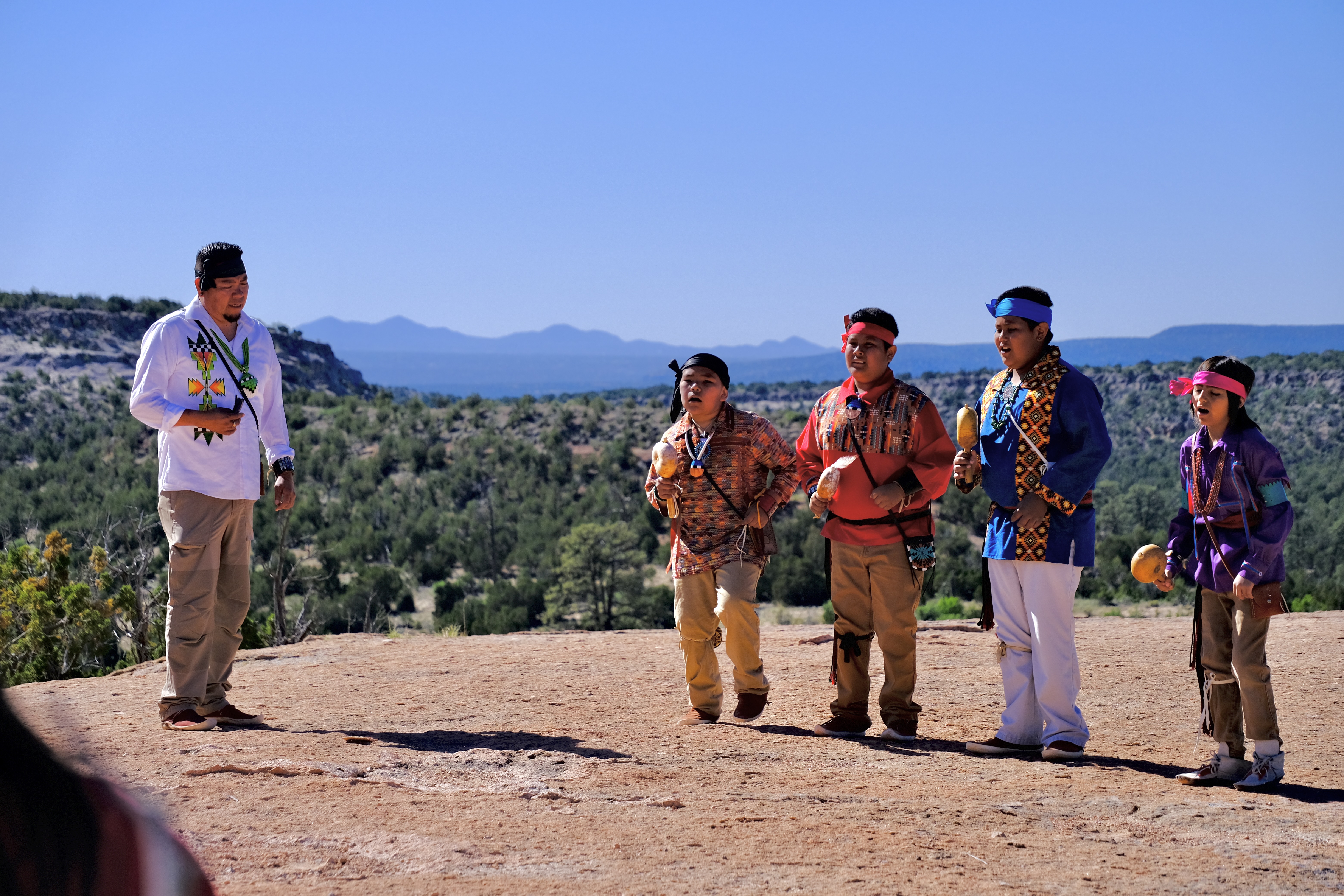 Dancers from the Pueblo of San Ildefonso at Tsankawi. A group of Native American dancers wearing brightly colored, traditional clothing dancing.