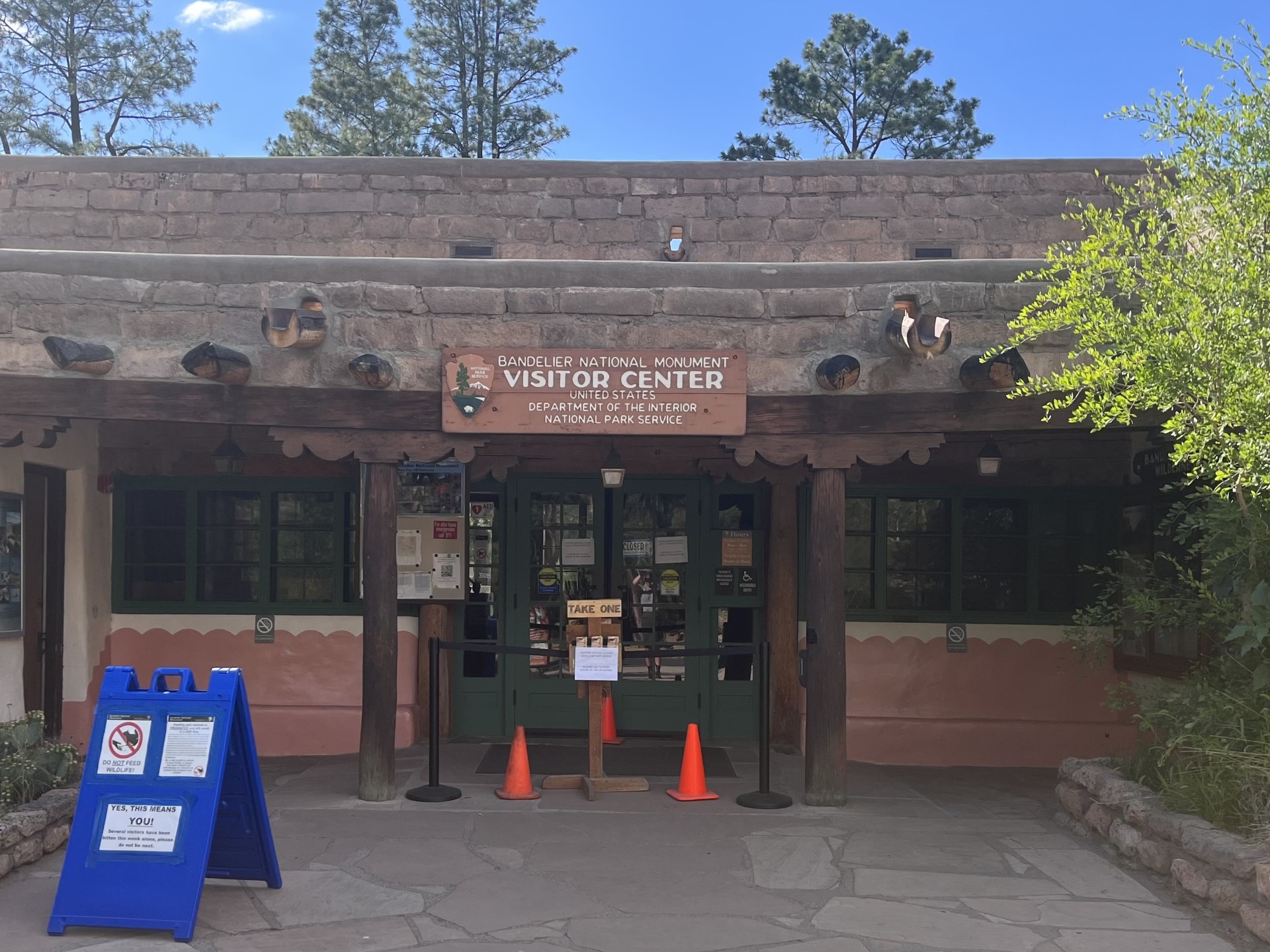 A stone building with green doors, which has orange cones set up in front of them. A stanchion blocks access to the building.