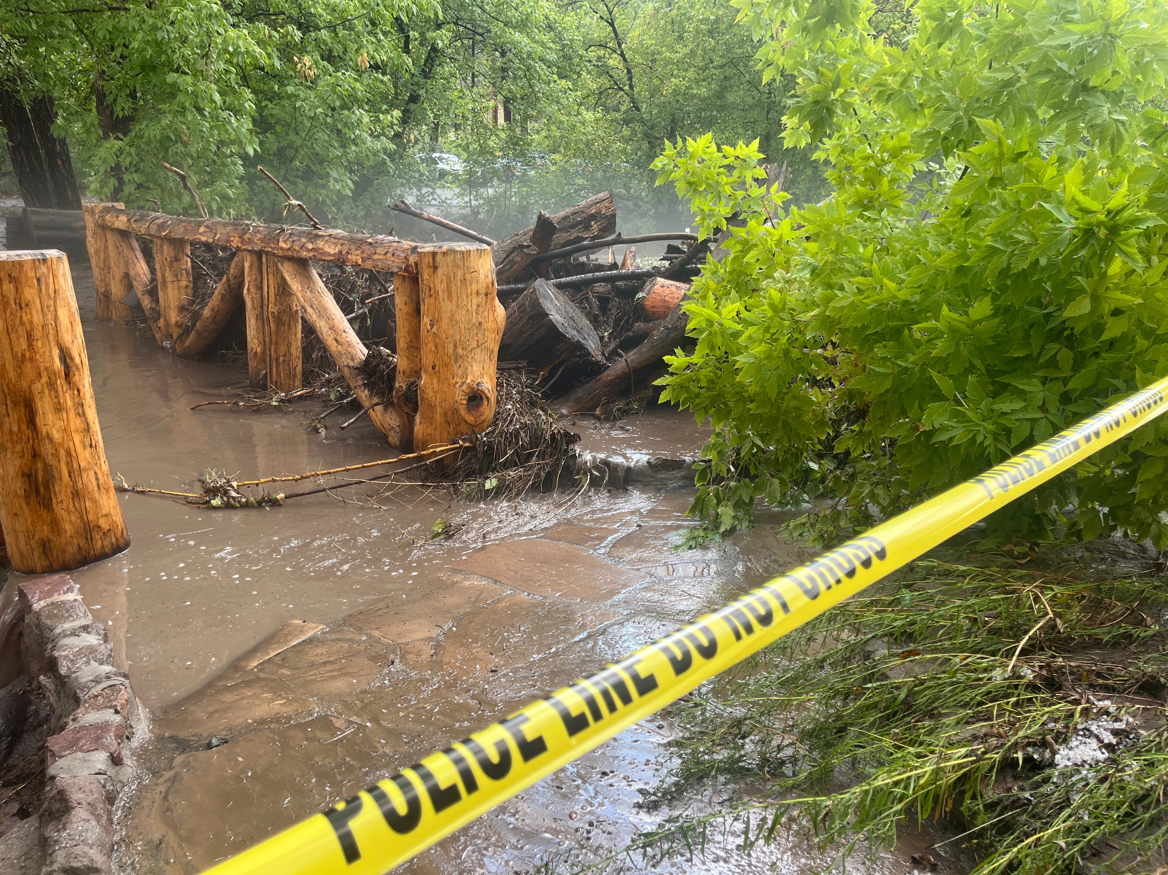 A wooden bridge with water running over it and surrounded by debris.