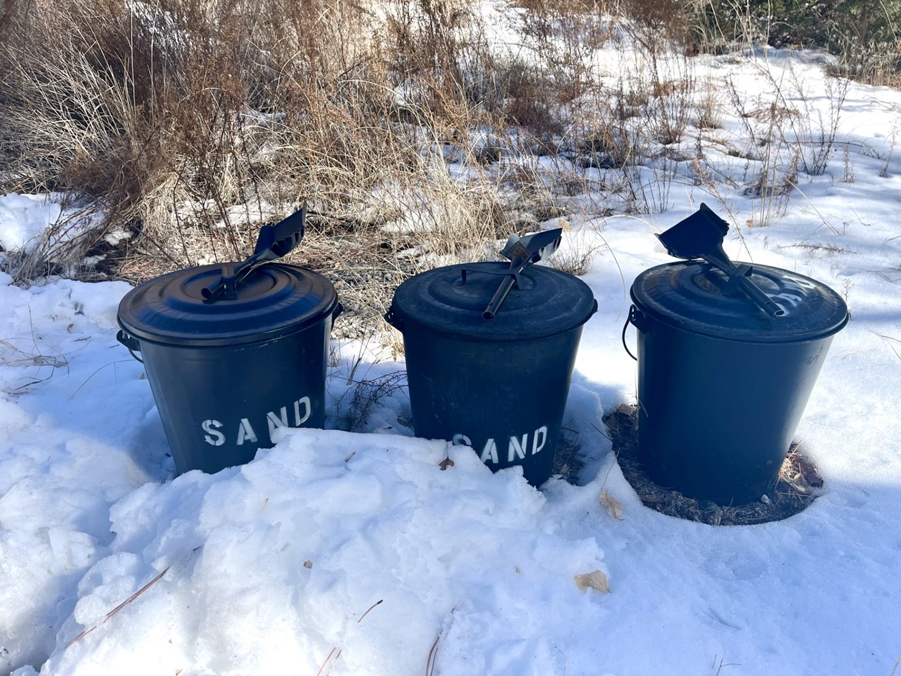 Three buckets marked "SAND" sitting in the snow.