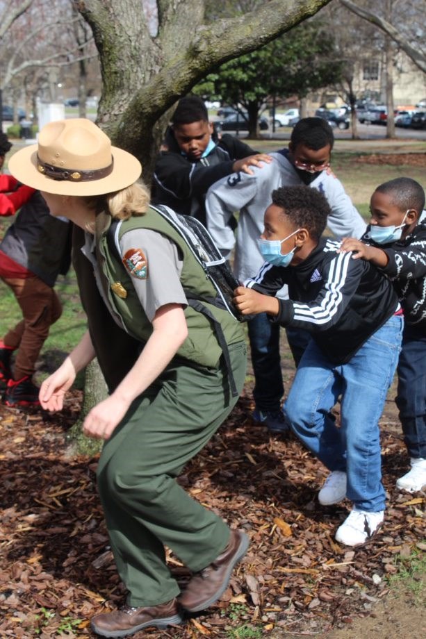 Ranger crouches down, with a single file line of 4th grade students following behind in a game of follow the leader