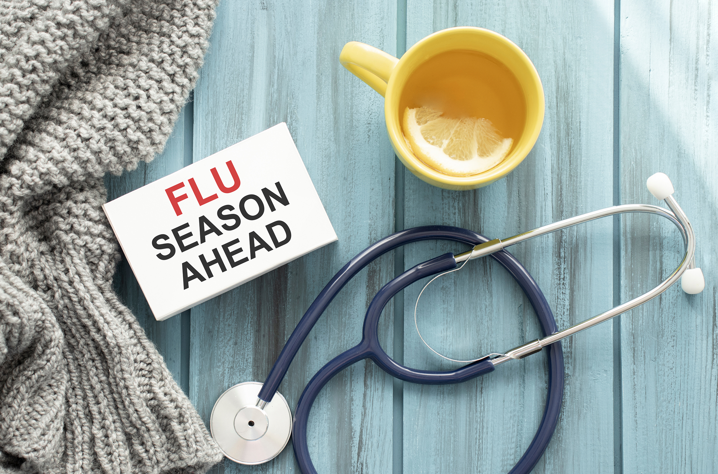 A stethoscope, tea, scarf, and a sign reading "Flu Season Ahead" on a blue background.