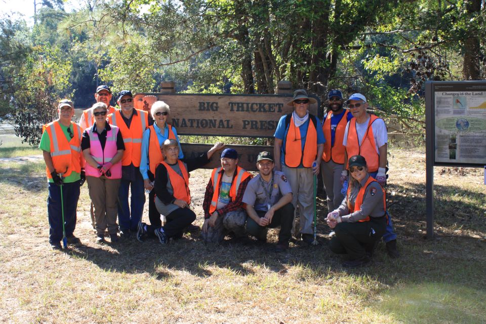 group of volunteers and rangers wearing orange vests while posing in front of a wooden sign